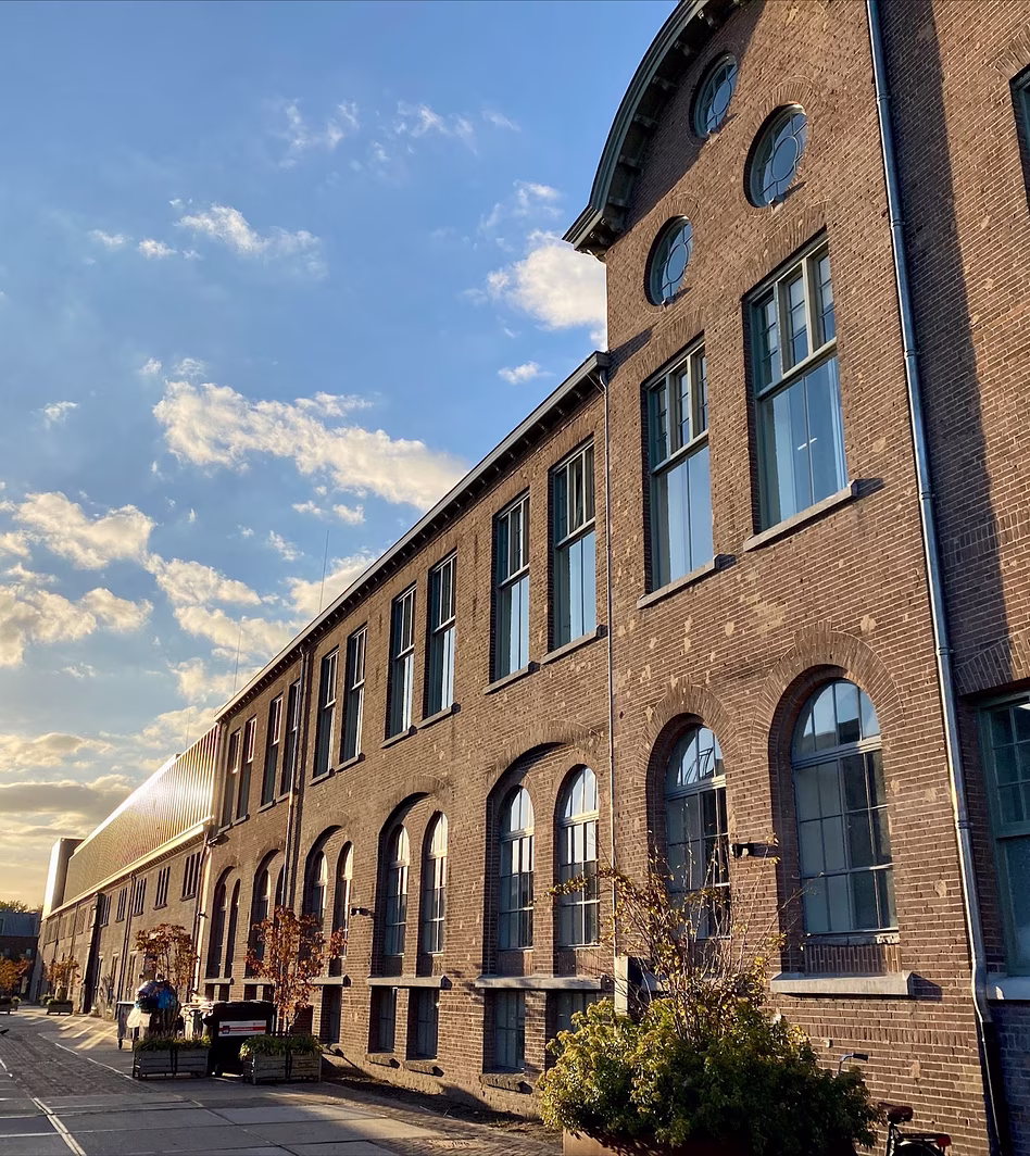 Rij bakstenen industriële gebouwen met grote blauwe ramen bij zonsondergang