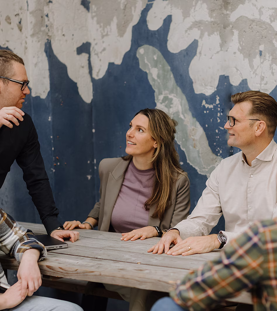 Groep mensen in gesprek aan tafel met bergachtige muurschildering op achtergrond