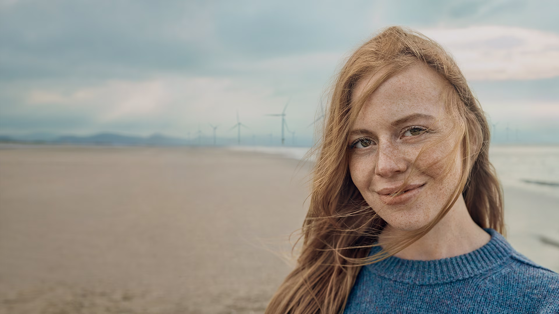 Glimlachende vrouw met rood haar op een strand met bewolkte lucht op de achtergrond
