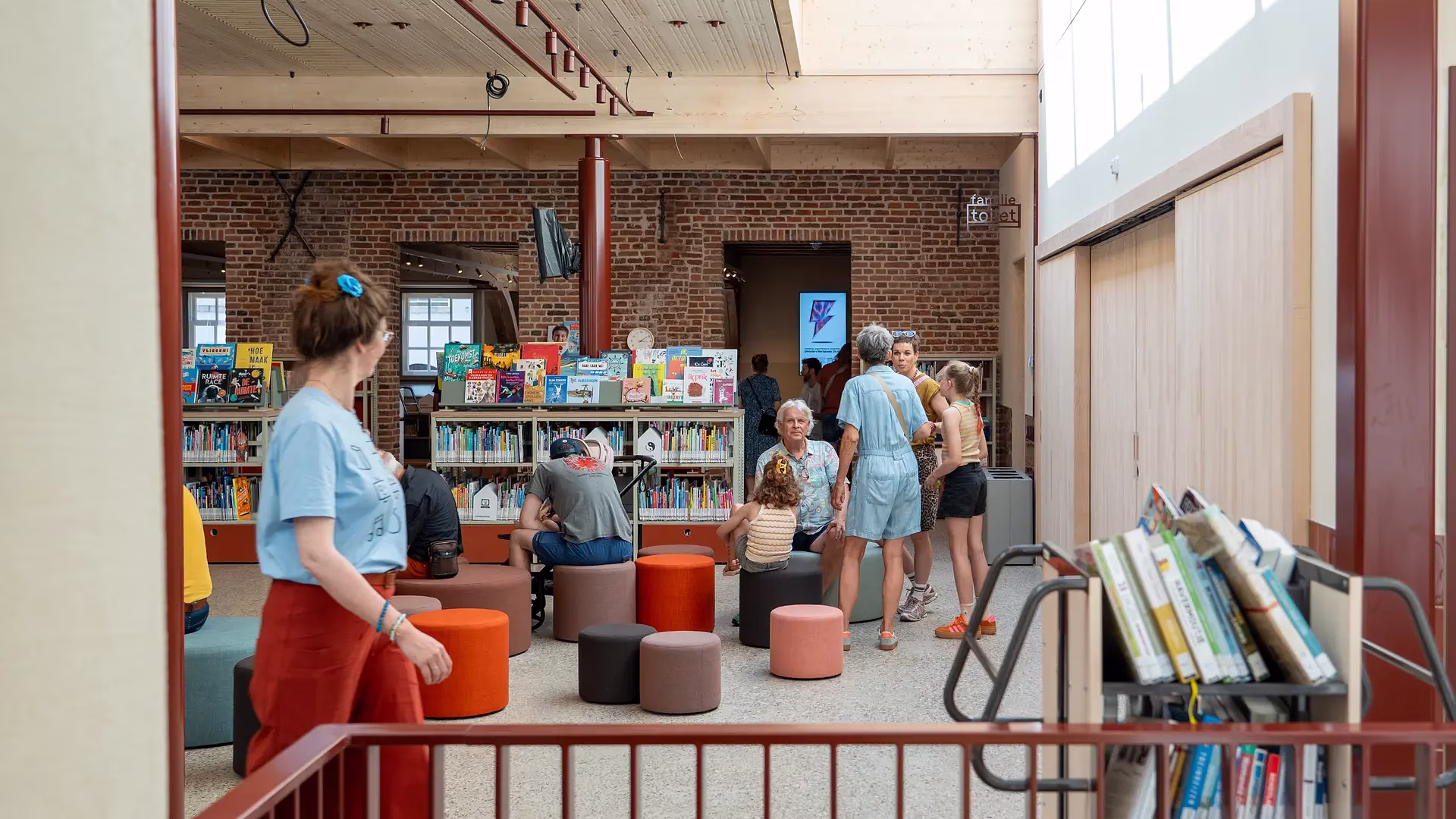Gezellige bibliotheek met klanten die rondkijken tussen boekenplanken en oranje stoelen