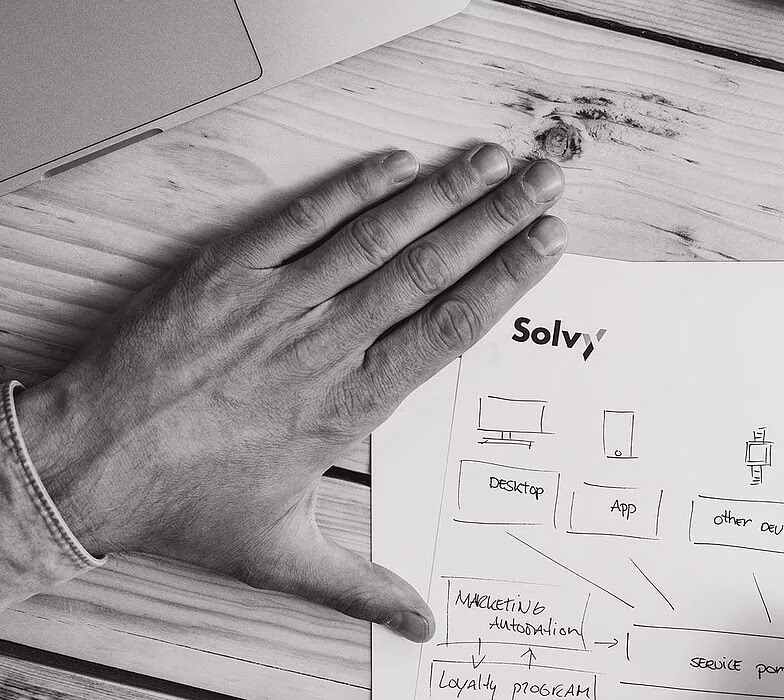 Hand schrijft met pen op papier met grafieken en laptop op tafel