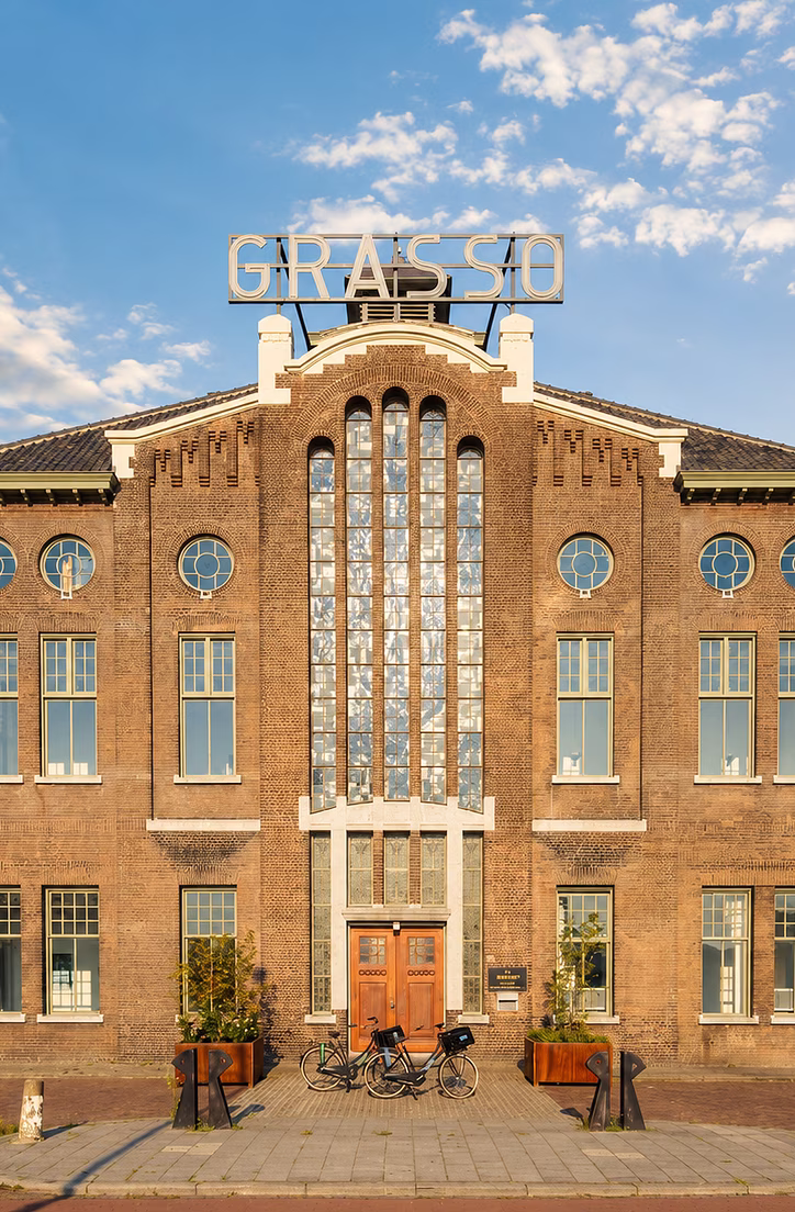 Historisch bakstenen gebouw met centrale ingang en klokkentorentje onder blauwe hemel