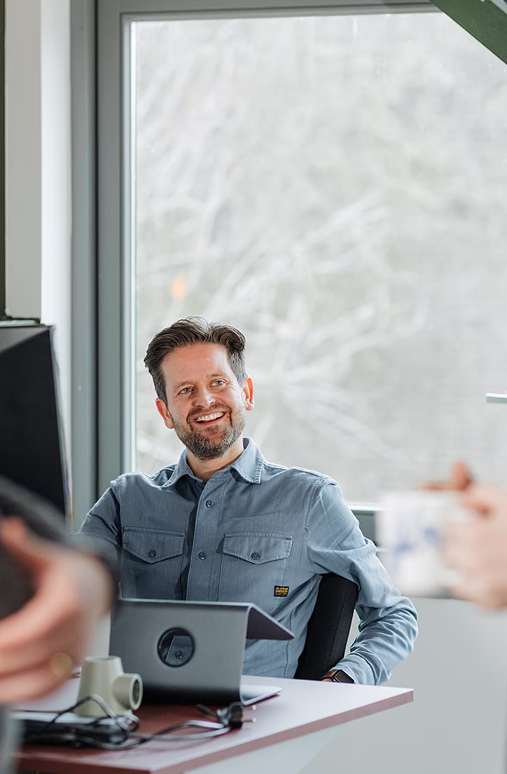 Man in spijkeroverhemd zit aan bureau en spreekt met twee staande collega's