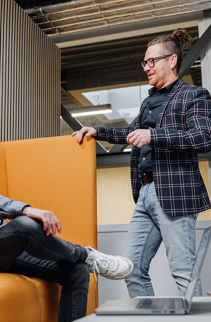 Twee mannen in gesprek bij een gele bank in een modern kantoor