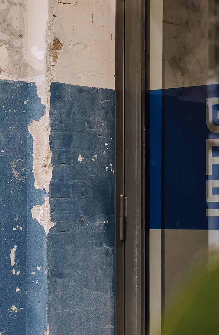 Verweerd blauw hout en een blauw bord met witte letters bij een deuropening
