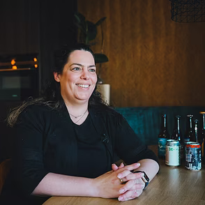 Glimlachende persoon zittend aan een bar met glazen op de toog