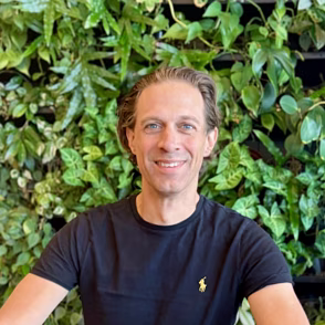 Man in donkerblauw shirt zittend voor groene plantenachtergrond